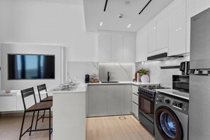 Une cuisine moderne équipée d’un lave-linge intégré, d’un grand téléviseur à écran plat et d’un coin repas avec des chaises.