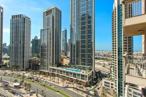 A high-rise building with a modern glass facade, a rooftop pool, and a busy street with palm trees.