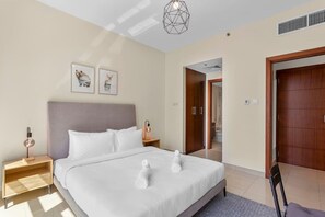 Een moderne hotelkamer met een groot bed, een houten hoofdbord, twee nachtkastjes met lampen, en een deur naar een andere kamer.