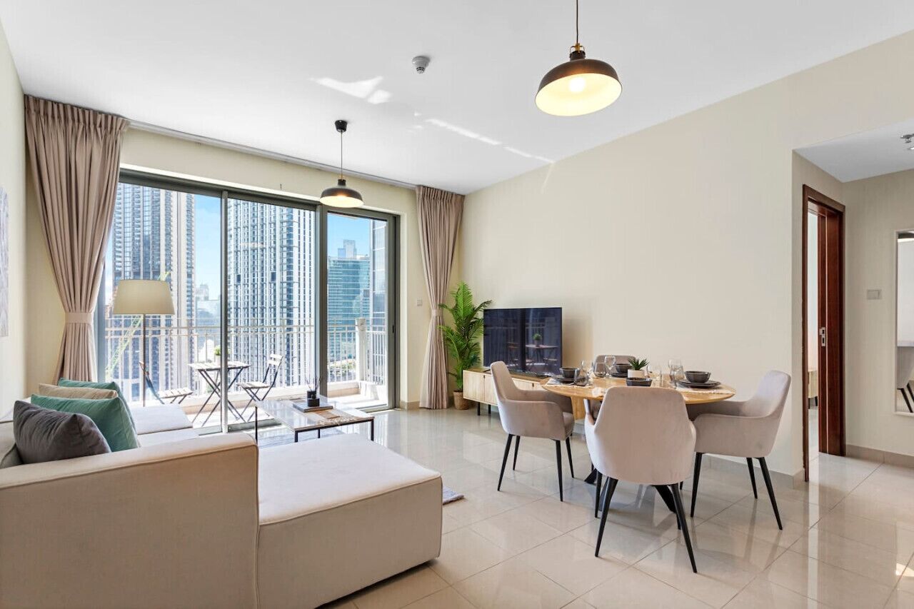 Un salon moderne avec un canapé, une table à manger et des chaises. Une grande fenêtre offre une vue sur de hauts immeubles.