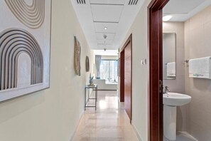 A hotel corridor with a modern design, a visible bathroom with a sink and towel, and a window providing natural light.