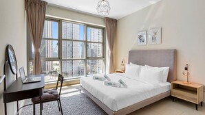 Ein Hotelzimmer mit großem Fenster, einem Bett mit weißer Bettwäsche, einem Schreibtisch mit Laptop und einem Nachttisch mit Lampe.