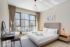 Una habitación de hotel con un ventanal grande, una cama con ropa de cama blanca, un escritorio con una computadora portátil y una mesita de noche con una lámpara.