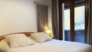 A bed with a quilted bedspread and two pillows, a bedside lamp, and a window with curtains. - Spacious T3 for 6 near slopes, comfortable, pets allowed (Les Orres)