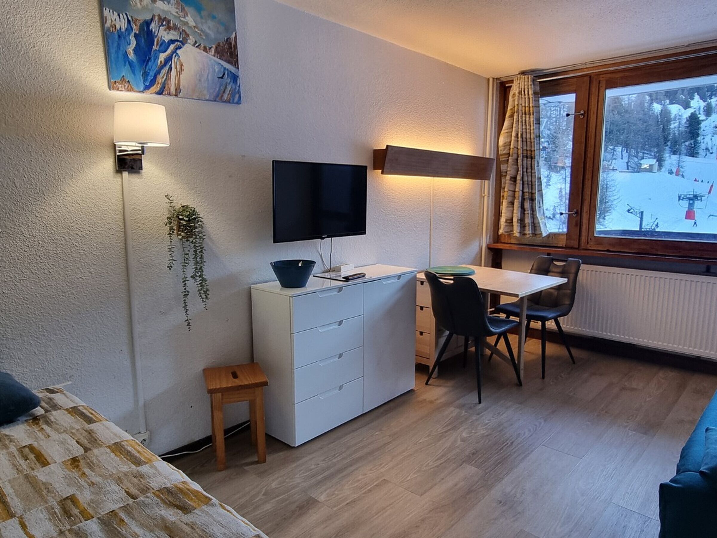 Une pièce confortable avec un lit, un bureau et une chaise, un téléviseur et une fenêtre donnant sur un paysage enneigé.