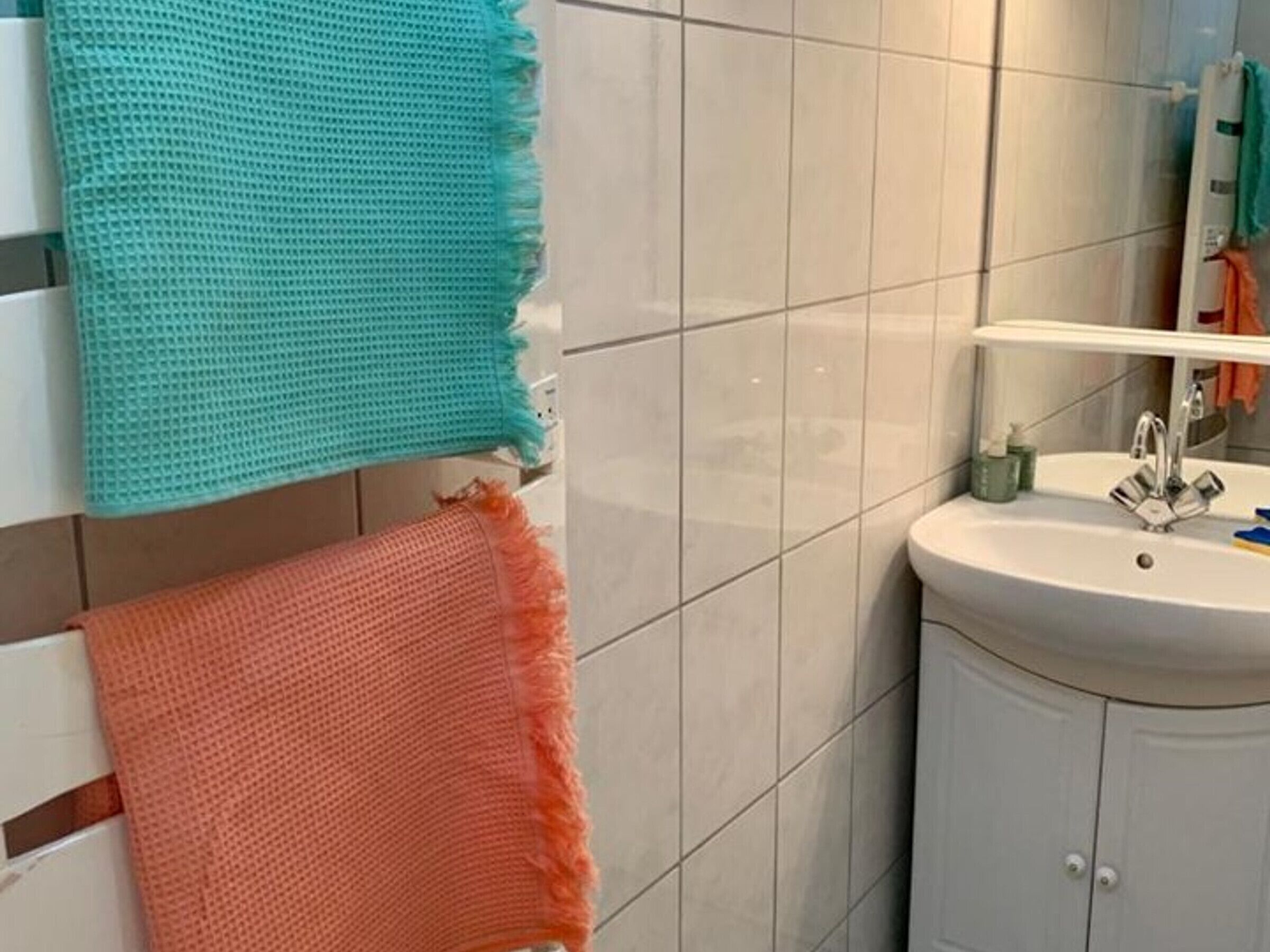 A bathroom with a white sink, a mirror, and a towel rack with two towels.