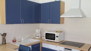 Eine kompakte Küche mit blauen Schränken, einer weißen Mikrowelle, einer Kaffeemaschine und einem Geschirrspüler.