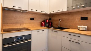 Eine kompakte Küche mit weißen Schränken, einer Holz Arbeitsplatte, einem eingebauten Ofen, einer Kaffeemaschine und einem Spülbecken.