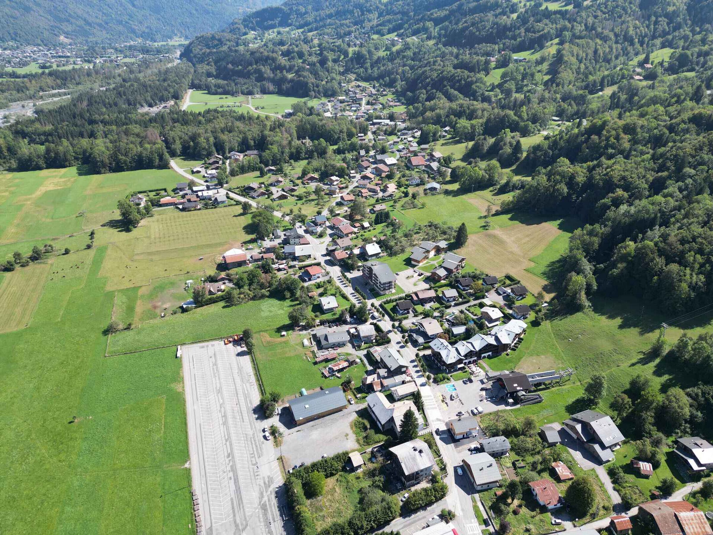 An aerial view of a village with houses, fields, and a large open area.