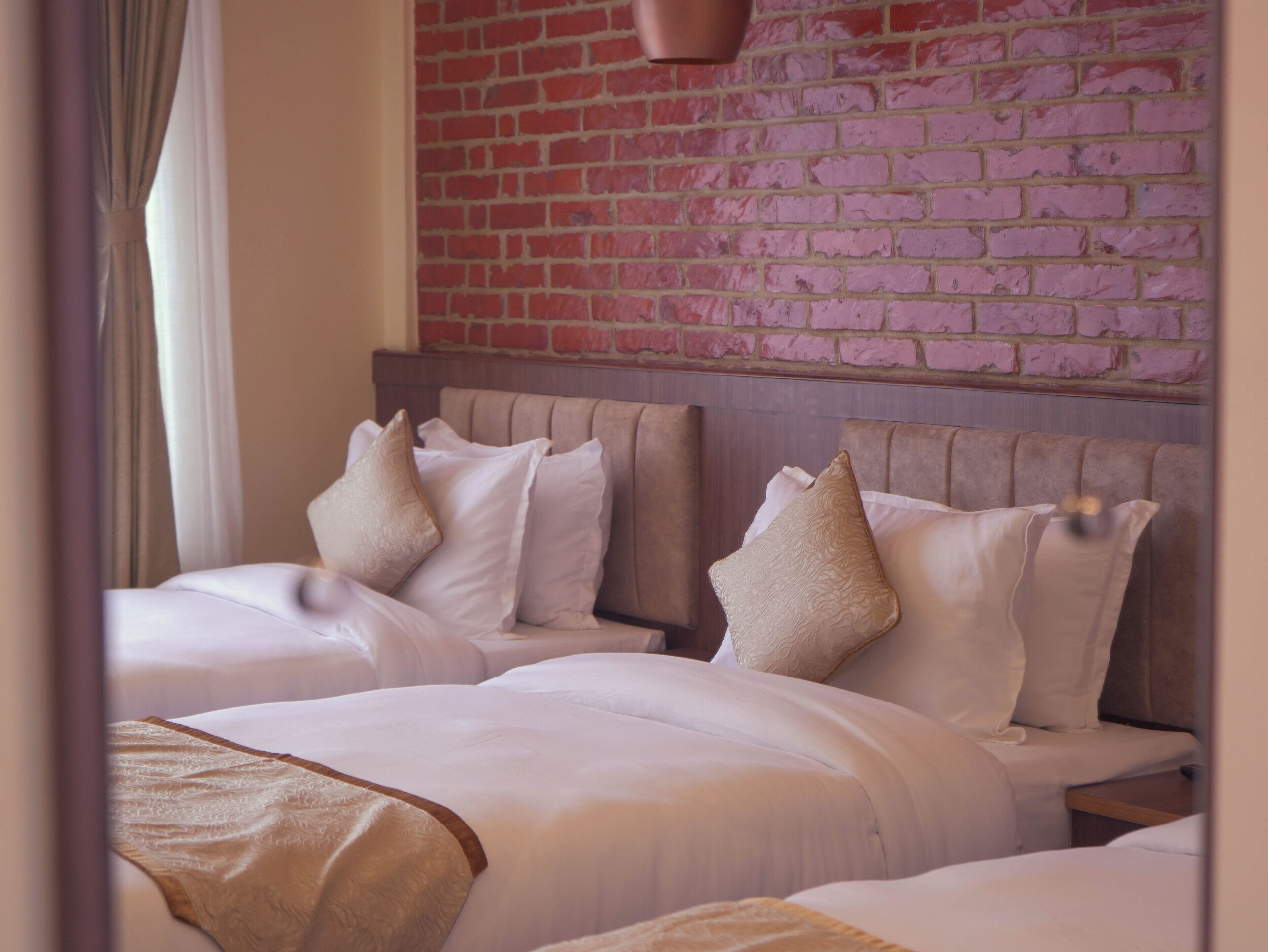A hotel room with two beds, a brick wall, and a hanging light fixture.