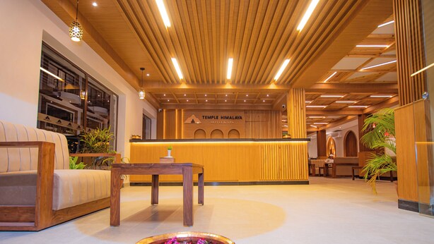 A reception area with a wooden reception desk, a sofa, a small table, and a decorative bowl with flowers. - Temple Himalaya Hotel & Spa (Pokhara)