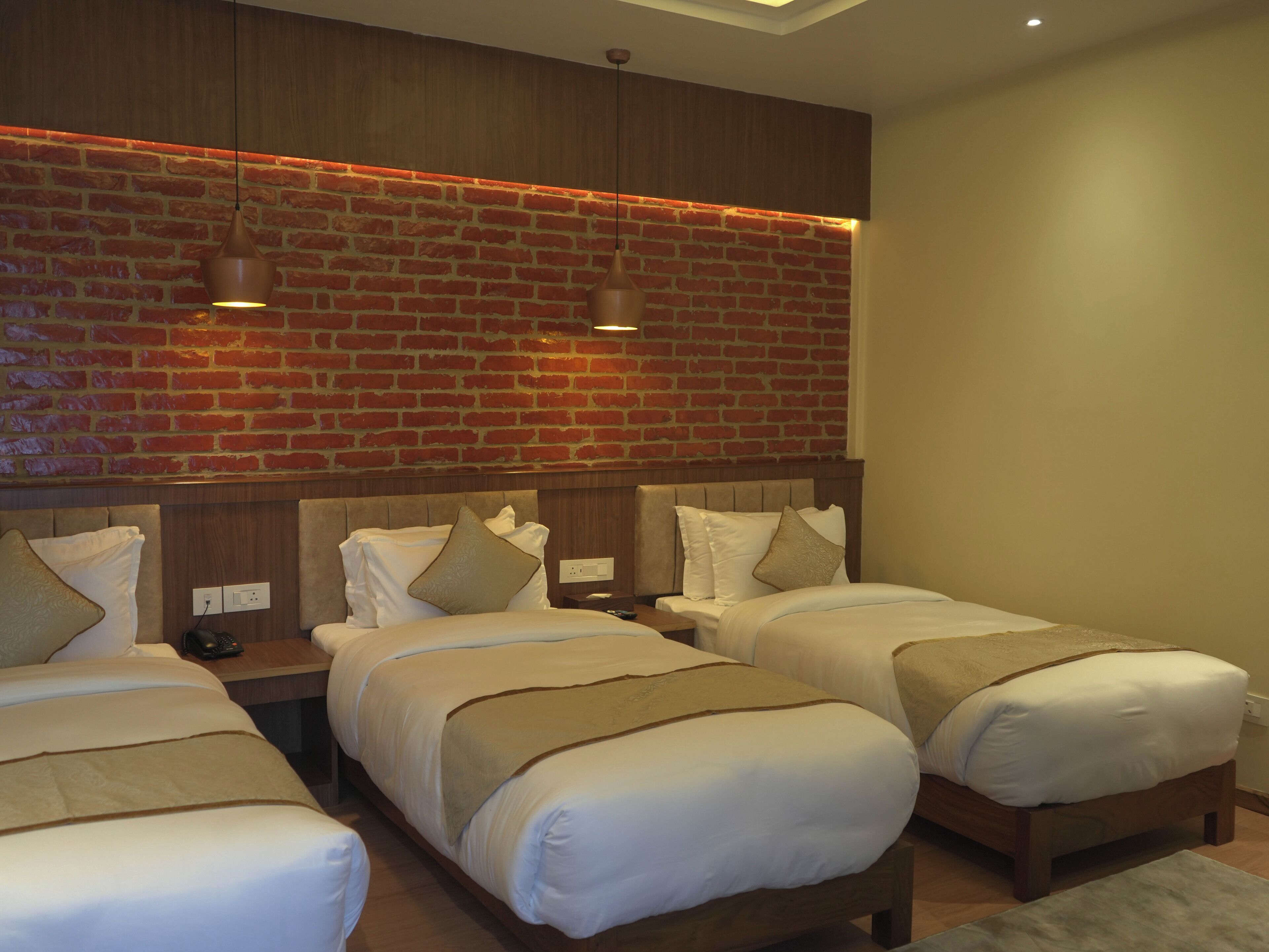 A hotel room with three single beds, a brick wall, and pendant lighting.