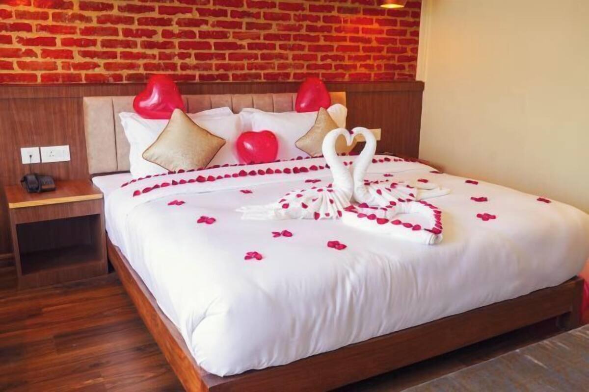 A hotel room with a brick wall, a wooden bed frame, and a neatly made bed with rose petals and a swan decoration.