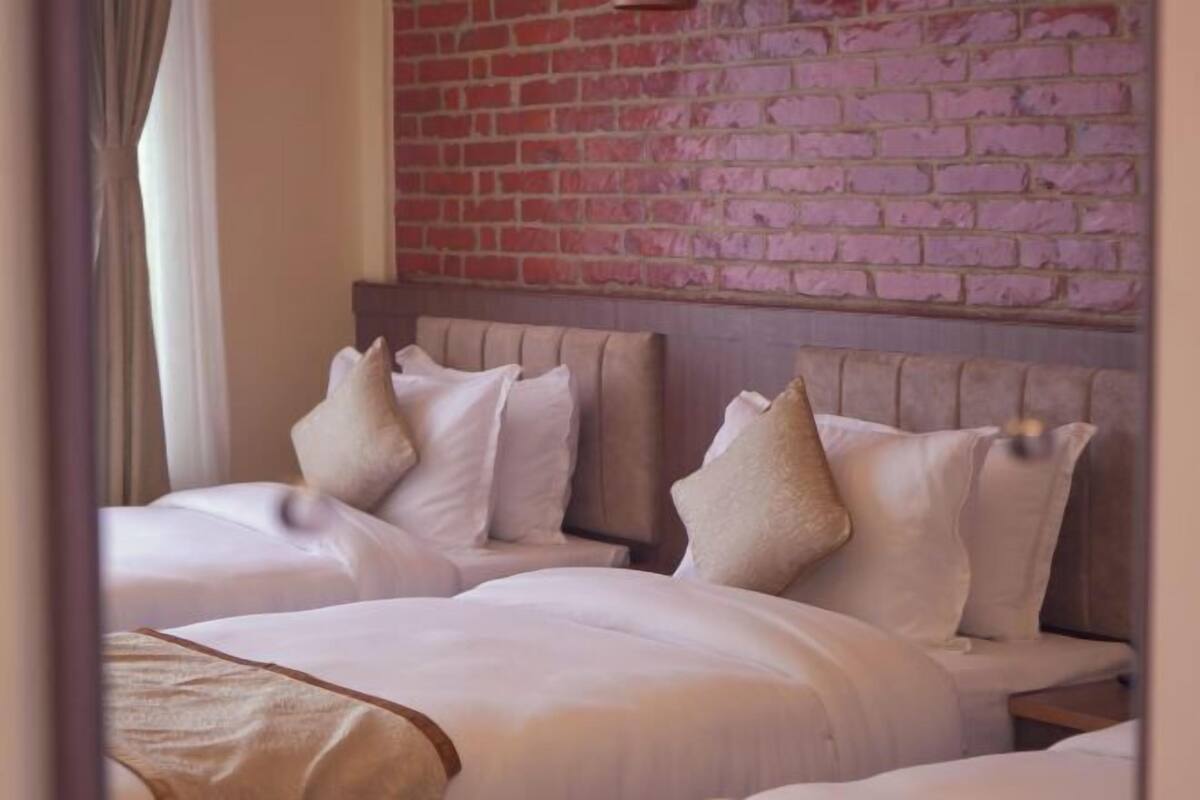 A hotel room with two beds, a brick wall, and a curtain.