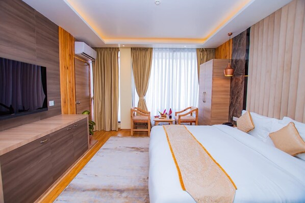 A modern hotel room with a large bed, a TV, a desk with chairs, and a wardrobe.