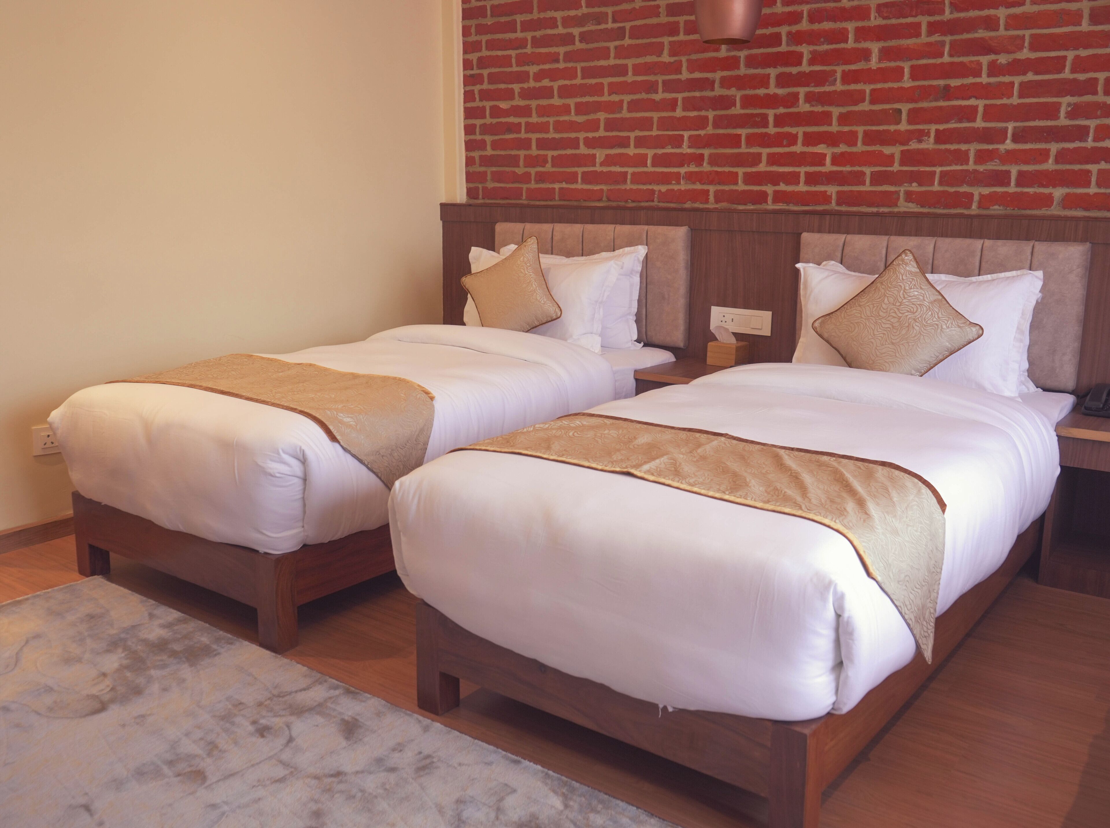 Une chambre d’hôtel avec deux lits simples, des têtes de lit en bois, un mur en briques et un sol en marbre.