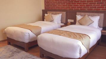 Une chambre d’hôtel avec deux lits simples, des têtes de lit en bois, un mur en briques et un sol en marbre.