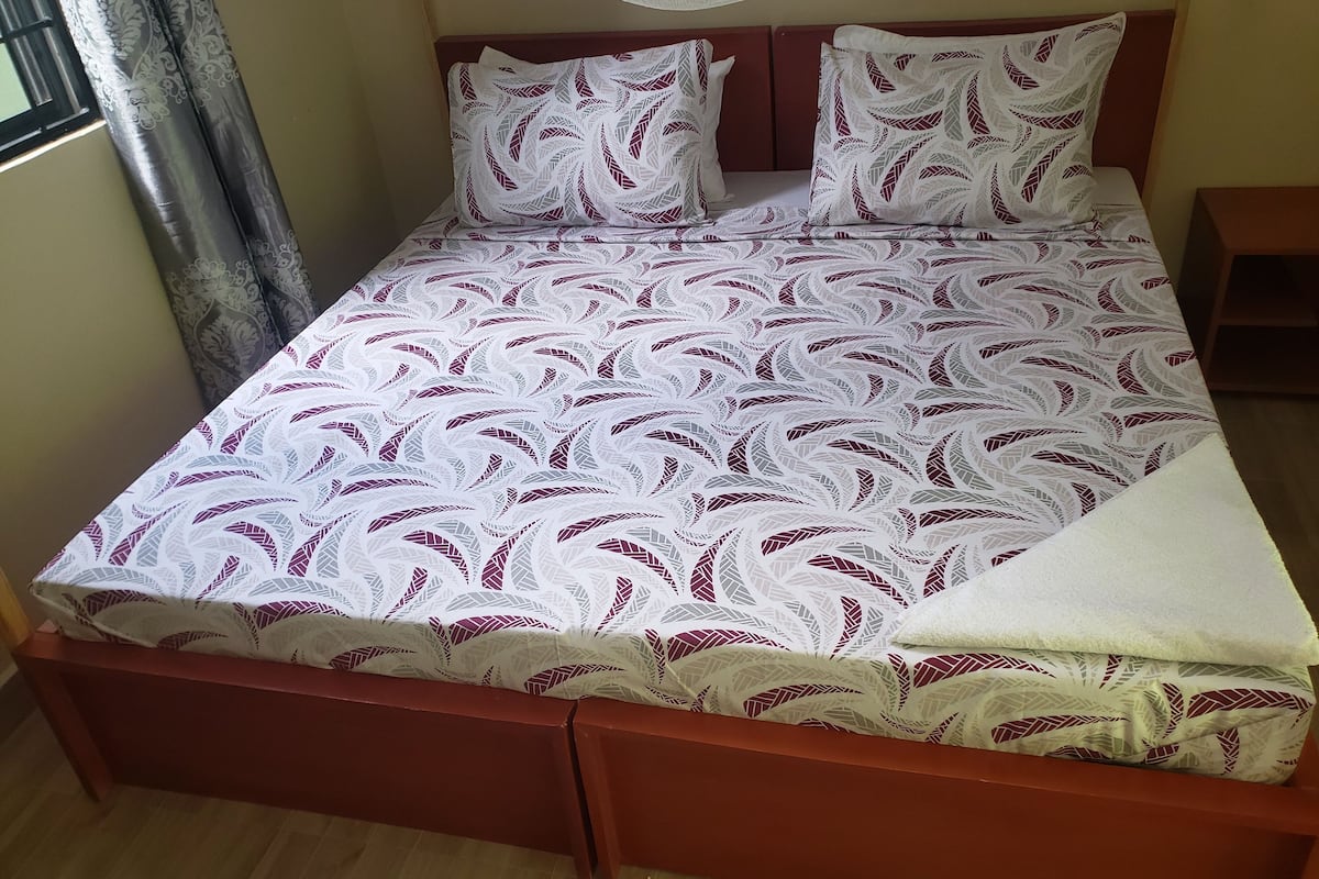 A bed with a patterned bedspread and pillows, a wooden headboard, and a bedside table.
