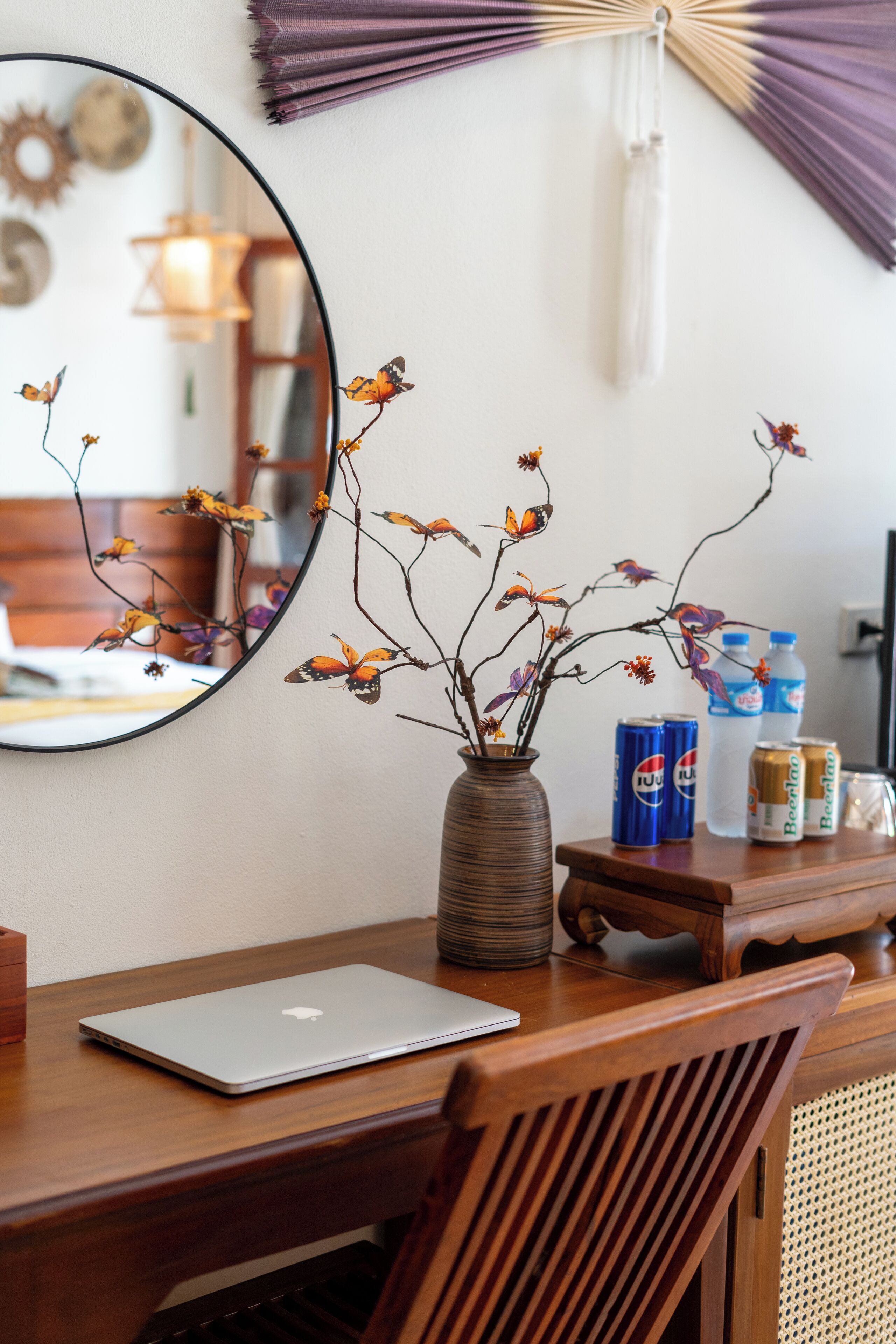 Un escritorio de madera con una computadora portátil, un florero con ramas y flores, y latas de bebidas.