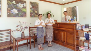 A reception area with wooden furniture, a desk with a vase of flowers, and framed artwork on the wall. - Elegant Boutique Hotel Luangpraban (Luang Prabang)