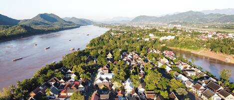 Uma cidade às margens do rio, com casas tradicionais, o rio e montanhas ao fundo.