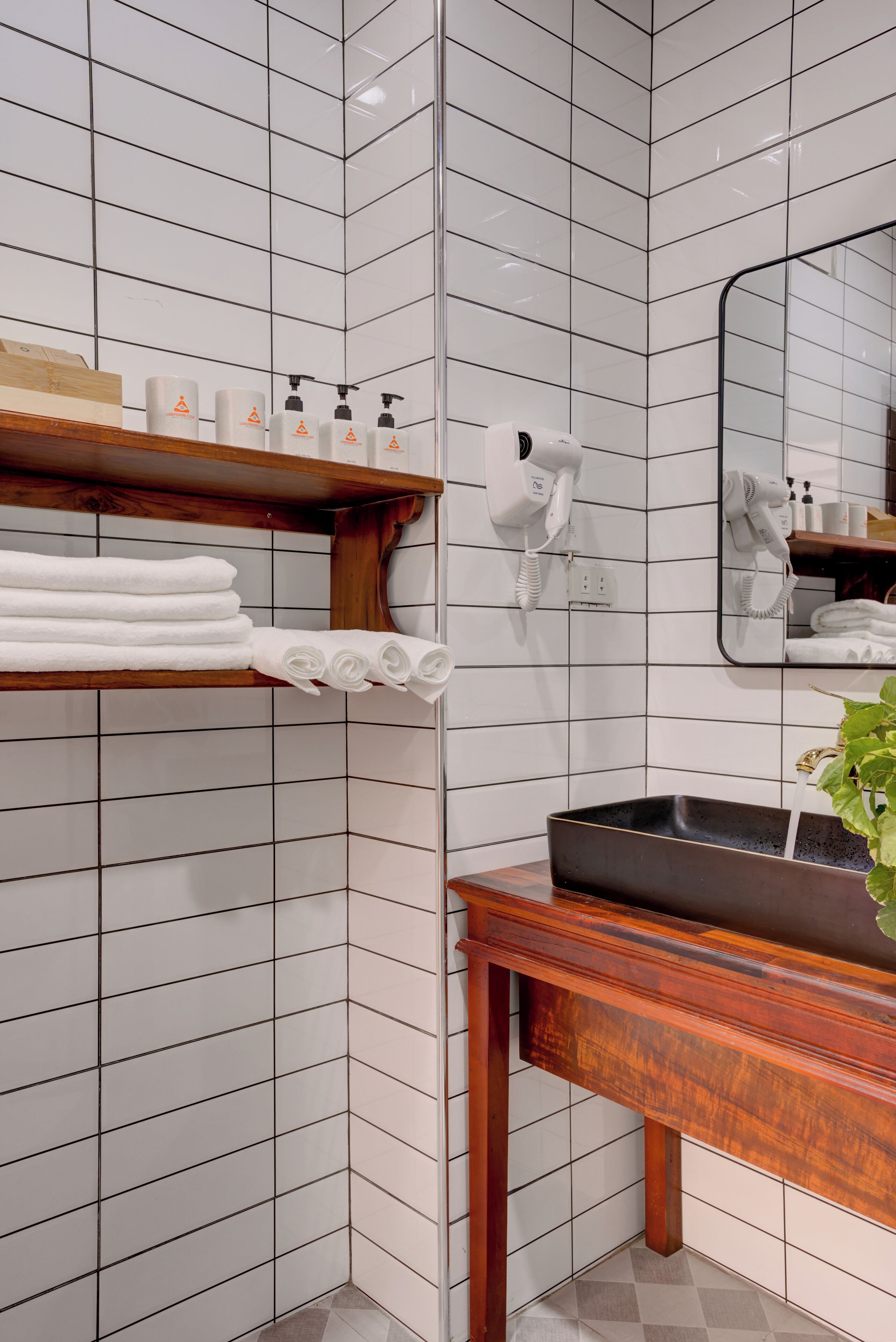 Un bagno con pareti in piastrelle bianche, uno scaffale in legno con asciugamani, un lavandino con una vasca nera e uno specchio.