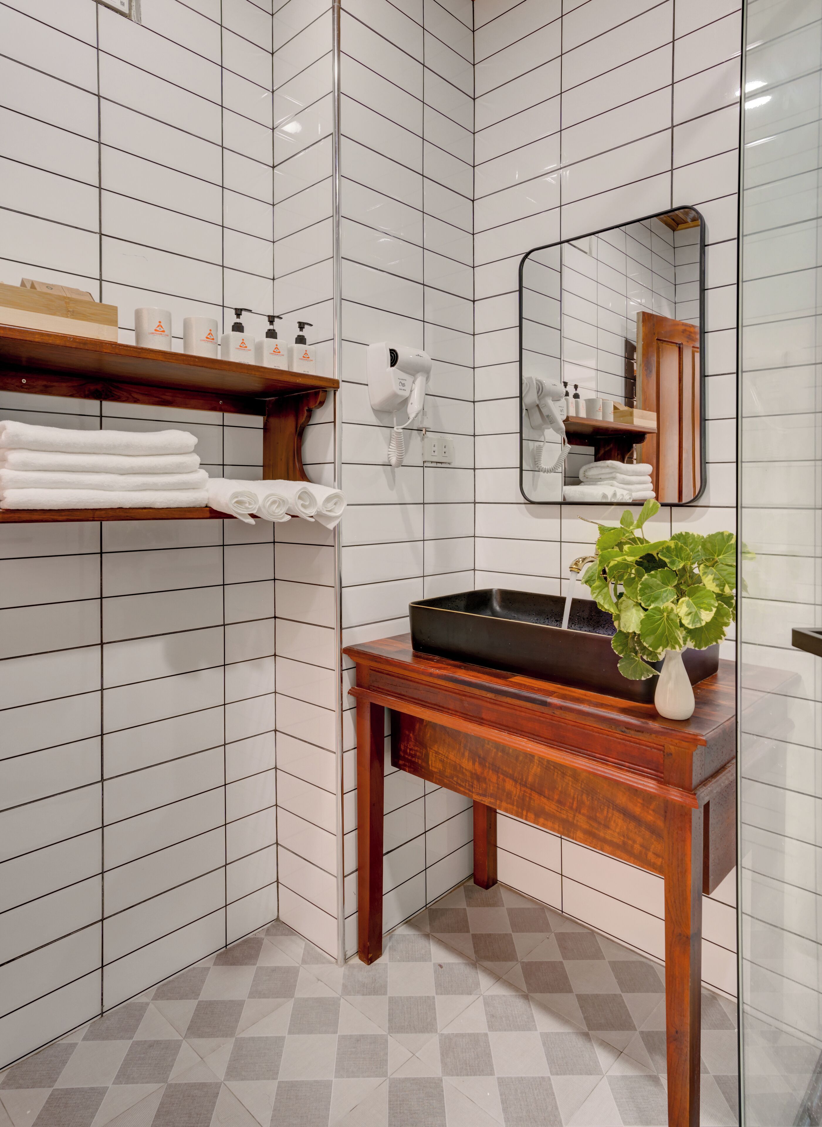 A bathroom with white tiled walls, a wooden vanity, a mirror, a sink, and a potted plant.