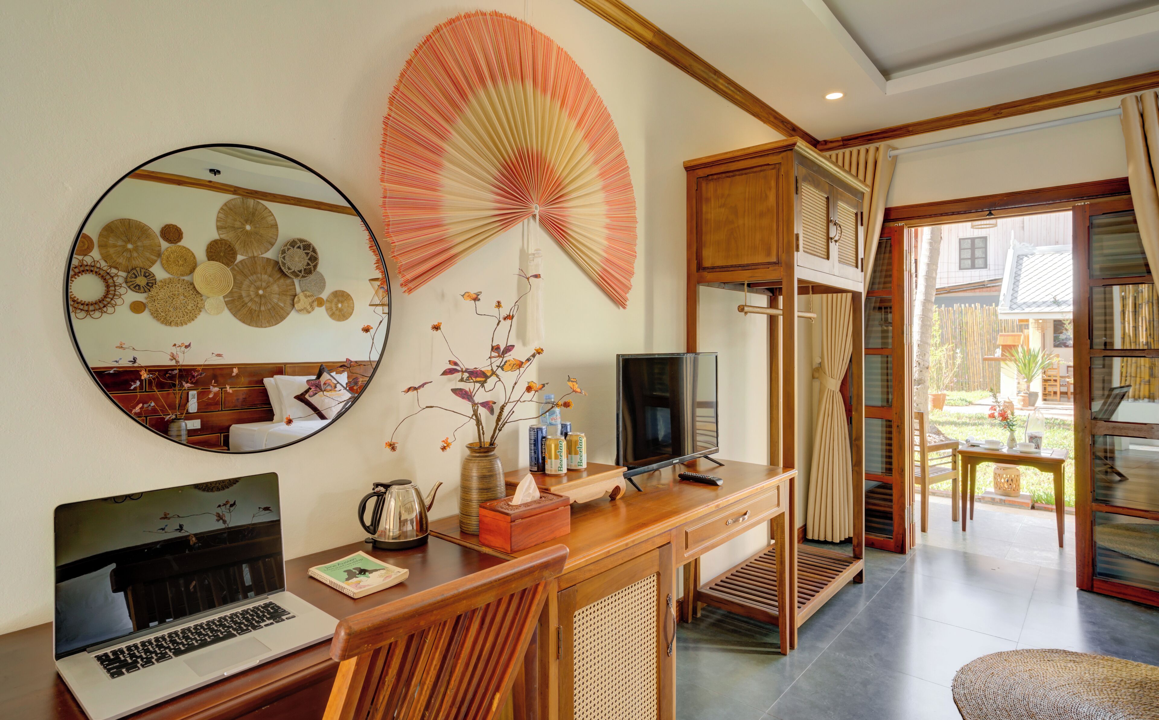 A well-lit room with a laptop on a wooden desk, a large mirror, and a traditional fan.