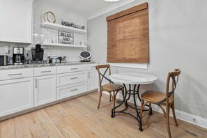 A kitchen with white cabinets, a round table, two wicker chairs, a coffee maker, and a sign on the wall. - Coastal Casa-Old Village-5 mins to Beach (Mount Pleasant)