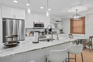 A modern kitchen with white cabinets, stainless steel appliances, and a marble island.
