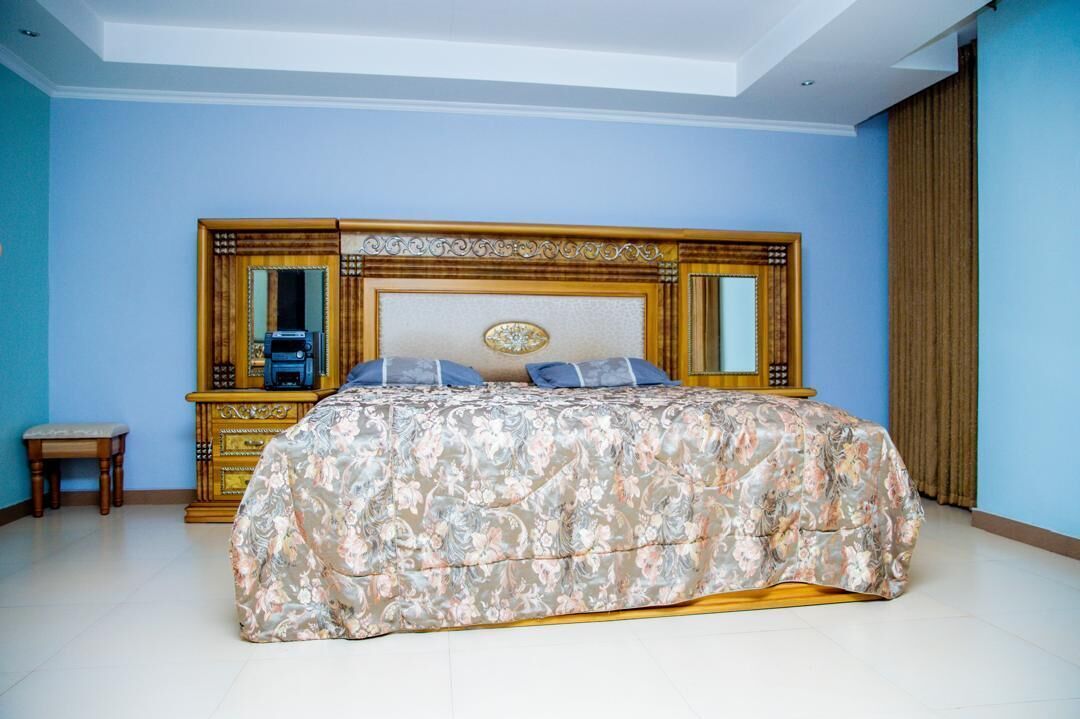 A bedroom with a large bed, a wooden headboard, a small bedside table, and a mirror.