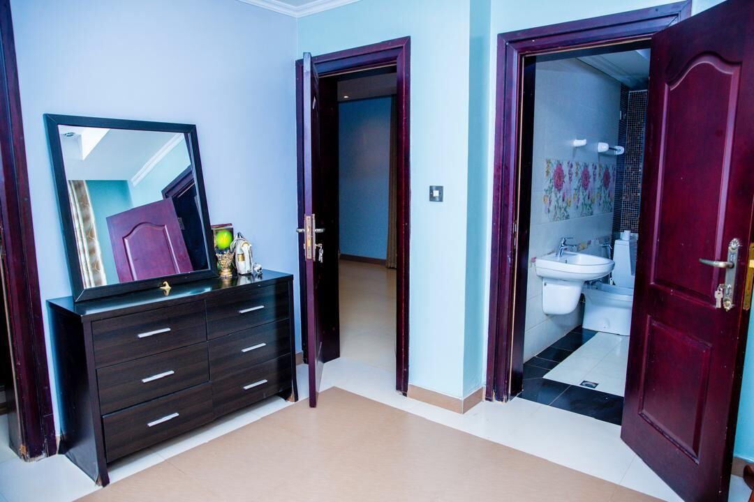 A room with a dark wooden dresser, a mirror, and an open door leading to a bathroom with a toilet and sink.