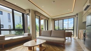 A modern living room with a sofa, a round coffee table, and a view of a cityscape through large windows.
