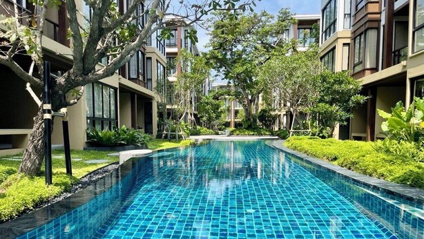 A swimming pool with a tiled surface, surrounded by greenery and modern buildings.