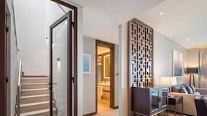 A modern living room with a sofa, a coffee table, and a TV stand. There is a staircase leading to another room. - Angsana Oceanview Residences by Banyan Living (Choeng Thale)