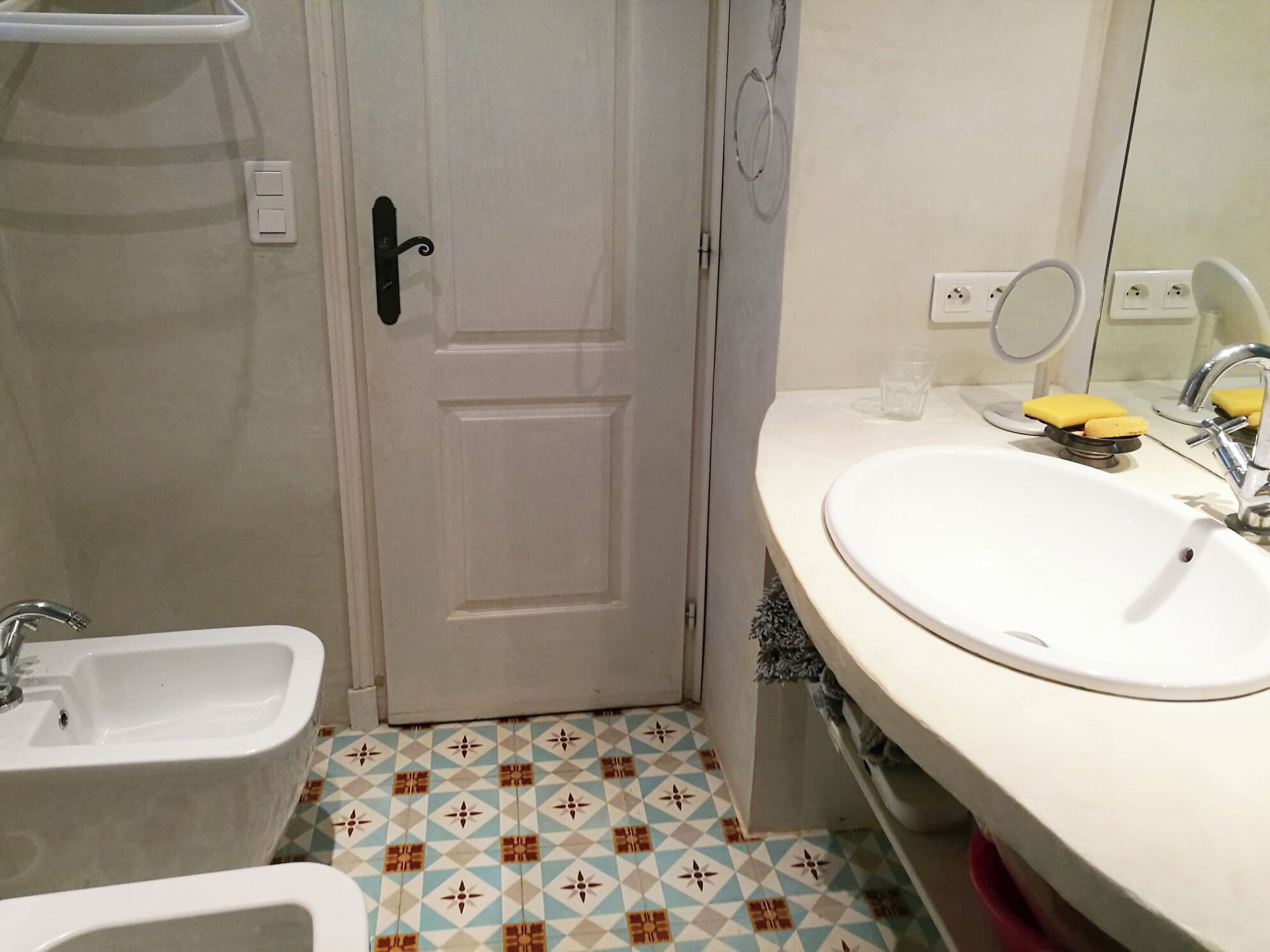 Casa de banho com lavatório branco, bidé e porta com puxador preto.