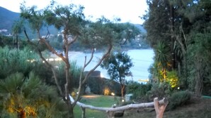 Ein Garten mit einer Holzbrücke, Bäumen und Blick auf das Meer.
