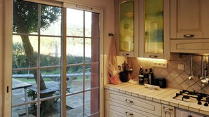 Eine Küche mit Gasherd, Backofen und Schränken. Ein Fenster bietet Blick auf eine Terrasse und einen Baum.