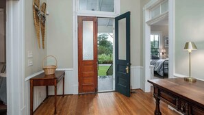 Un couloir avec un plancher en bois, une porte en bois, un panier en osier posé sur une table et une lampe.