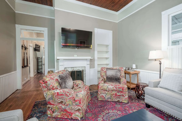 A living room with two patterned armchairs, a sofa, a fireplace, and a television mounted above it.