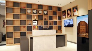 A modern interior with a wooden shelving unit displaying clocks and framed photographs, a marble reception desk, and a large television screen. - sun view hotel (Tabuk)