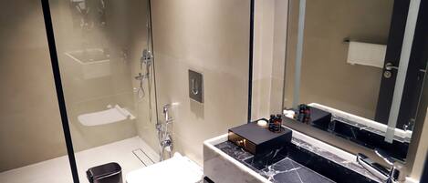 A modern bathroom with a glass shower enclosure, a white toilet, a black marble sink, and a large mirror.