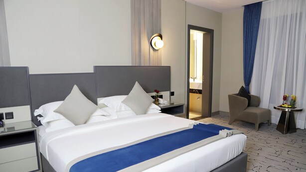 A hotel room with a large bed, a nightstand, a chair, a small table with a vase, and a mirror. - sun view hotel (Tabuk)