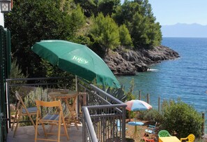 A terrace with outdoor seating, a green umbrella, and a view of the sea and rocky coastline. - Holiday Home Jadranka (Jelsa)