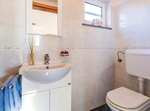 Ein Badezimmer mit weißem Waschbecken, einem Spiegel, einer Toilette und einem kleinen Fenster.