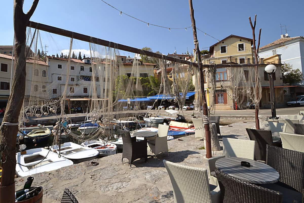 A marina with boats docked, outdoor seating, and buildings in the background.