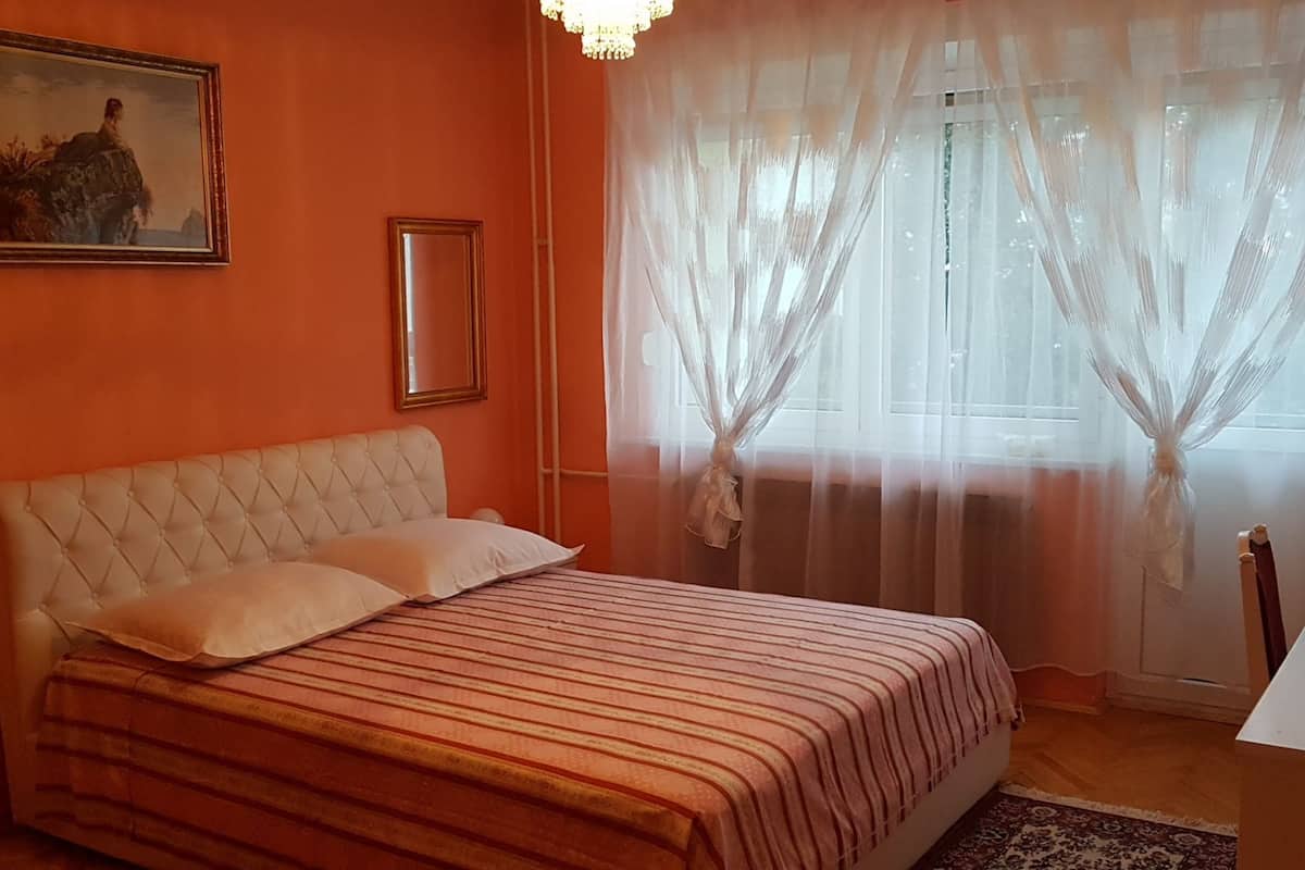 A bedroom with a bed, a painting on the wall, and sheer curtains on the window.