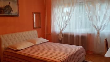 Un dormitorio con una cama, un cuadro en la pared y cortinas traslúcidas en la ventana.