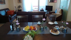 En spiseplads med et bord dækket til fire personer, med frugtfade, blomster og en tekedel.