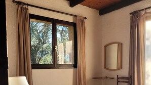 Une chambre à coucher comprenant un lit, une table de chevet, une chaise, une petite table, un miroir et une fenêtre avec des rideaux.